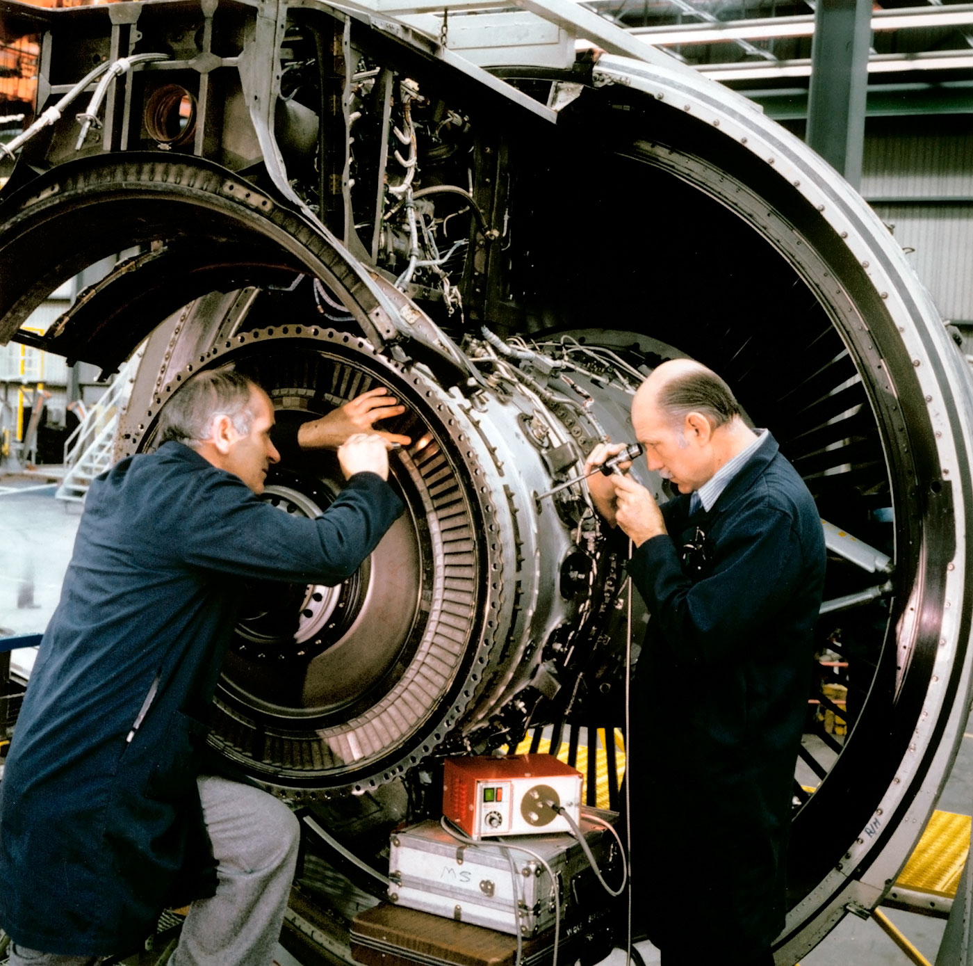 Two older male engineers working on an engine.